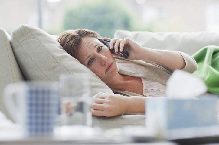 Sick woman laying on sofa talking on telephone